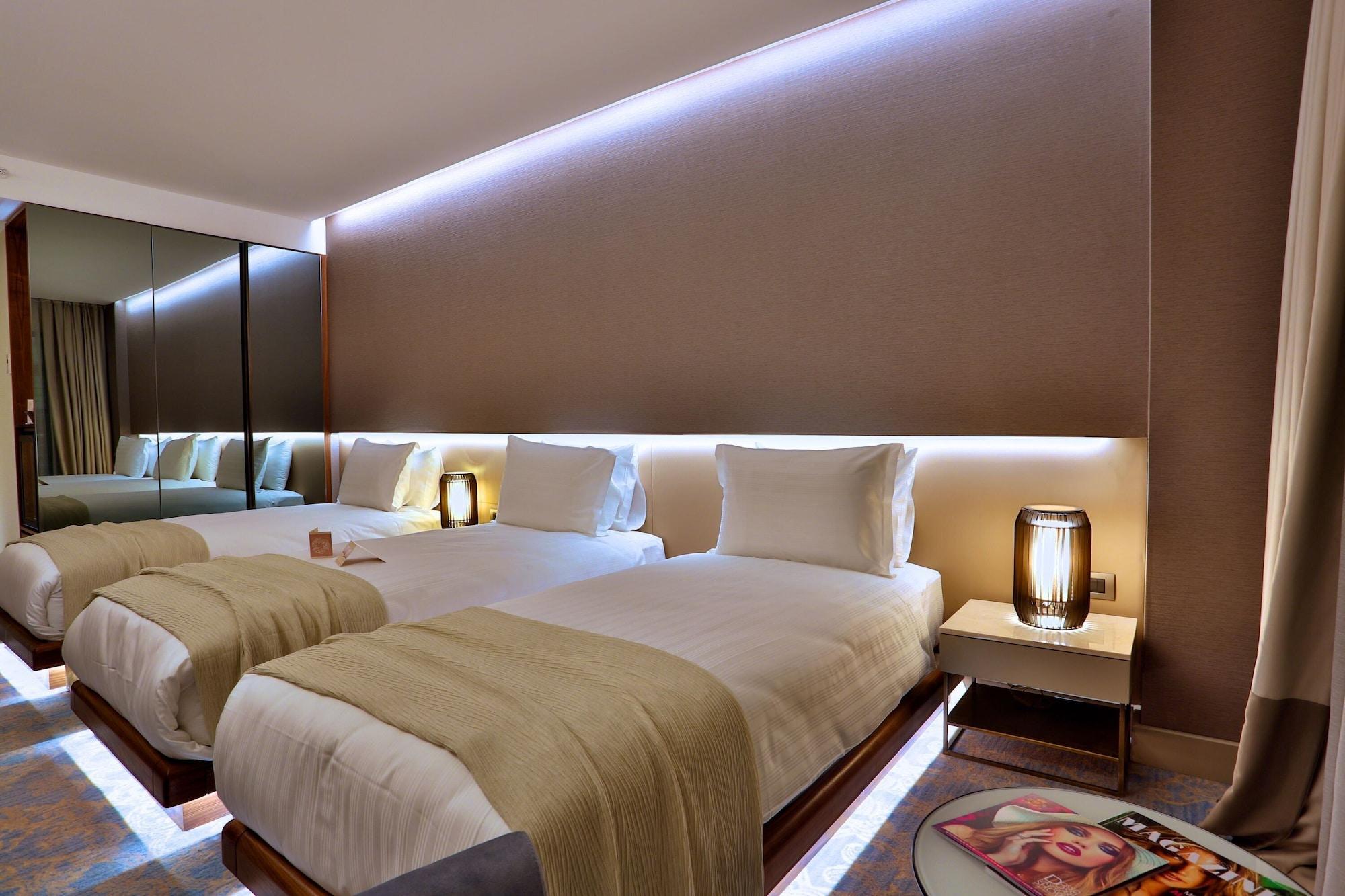 Dosso Dossi Hotels & Spa Downtown Istambul Exterior foto The photo shows a modern hotel room with two neatly made beds. Each bed is dressed with white linens and has a light-colored throw blanket. There are stylish bedside lamps on either side of the beds, as well as small nightstands. The wall behind the 