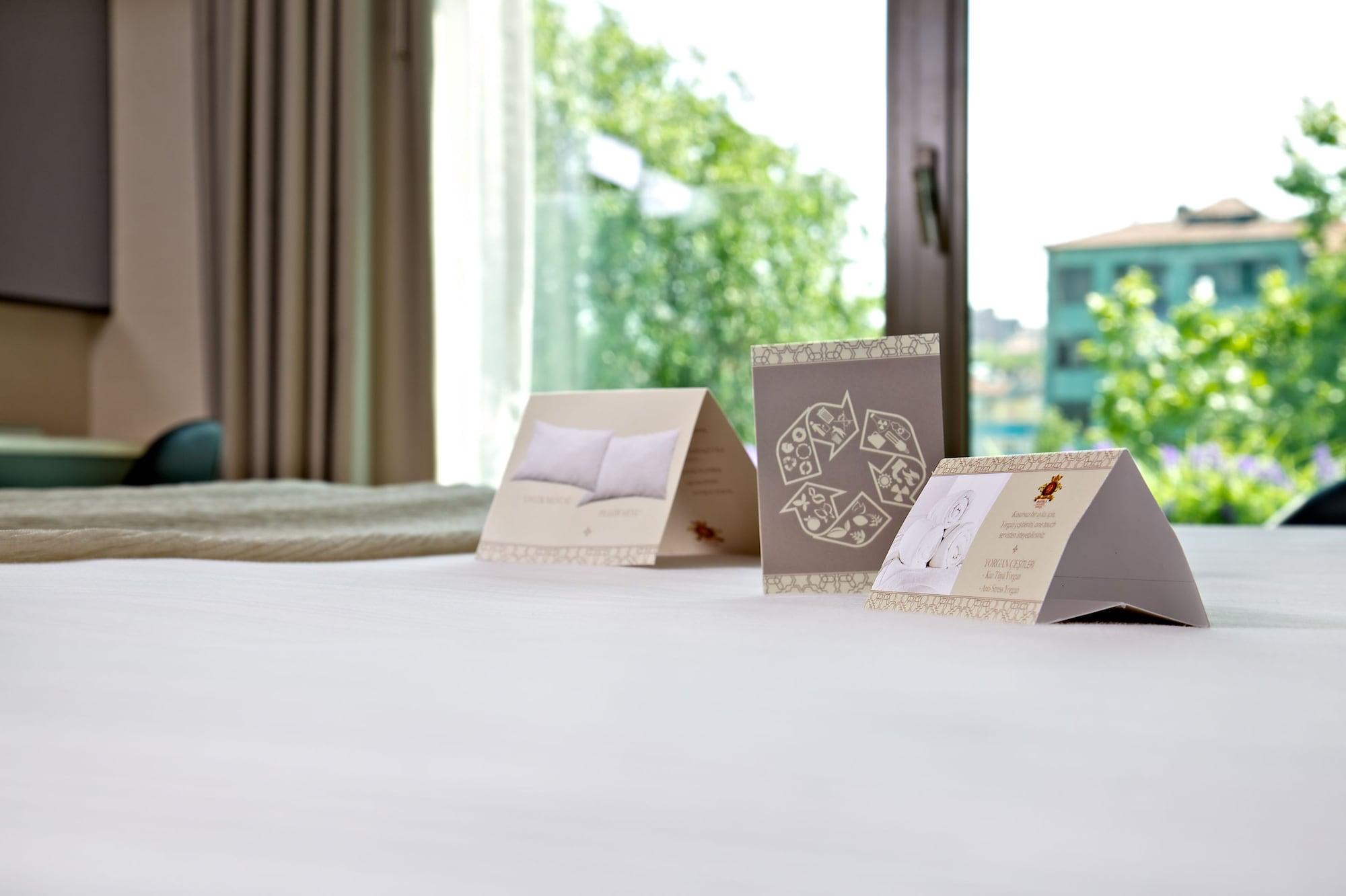 Dosso Dossi Hotels & Spa Downtown Istambul Exterior foto The photo shows a neatly made bed with a soft, white bedspread. In the foreground, there are three triangular cards placed upright on the bed. Each card has different designs or text, with one appearing to feature a pillow image and another possibly 