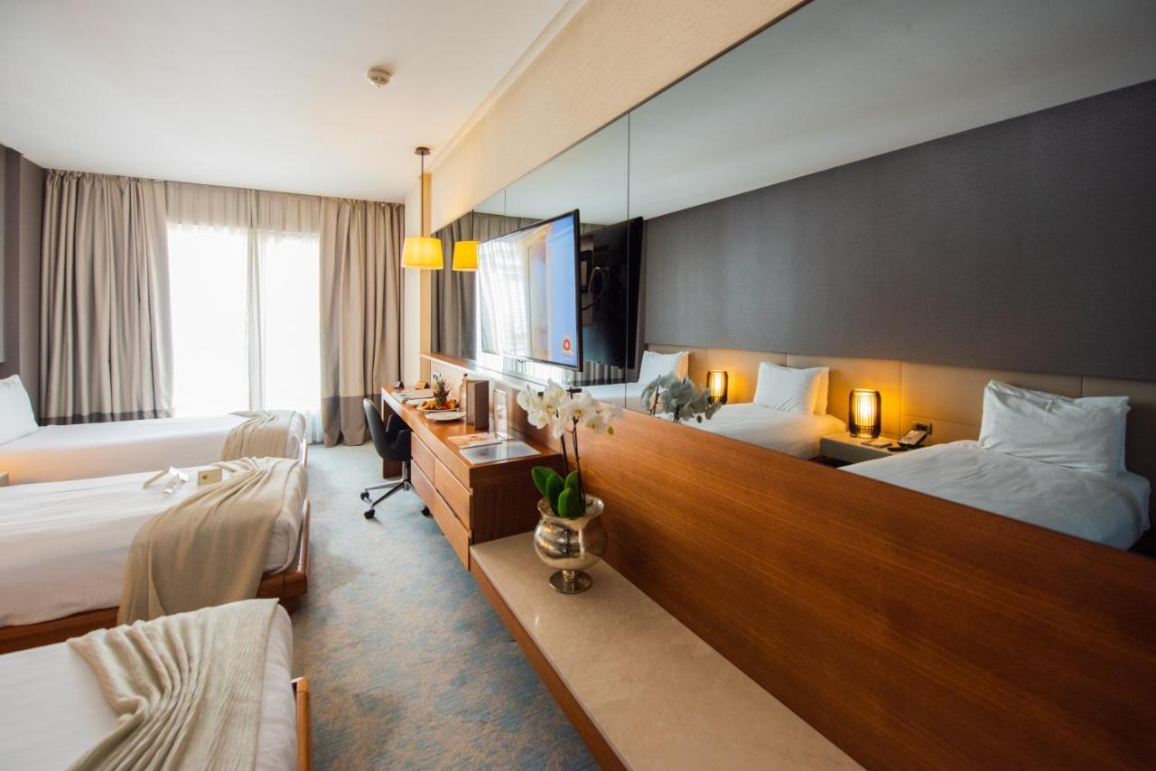 Dosso Dossi Hotels & Spa Downtown Istambul Exterior foto The photo shows a modern hotel room featuring two beds with light-colored bedding. There is a large mirror above a wooden dresser, which holds some decorative items, including a small plant. A TV is mounted on the wall, and there is a workspace with 