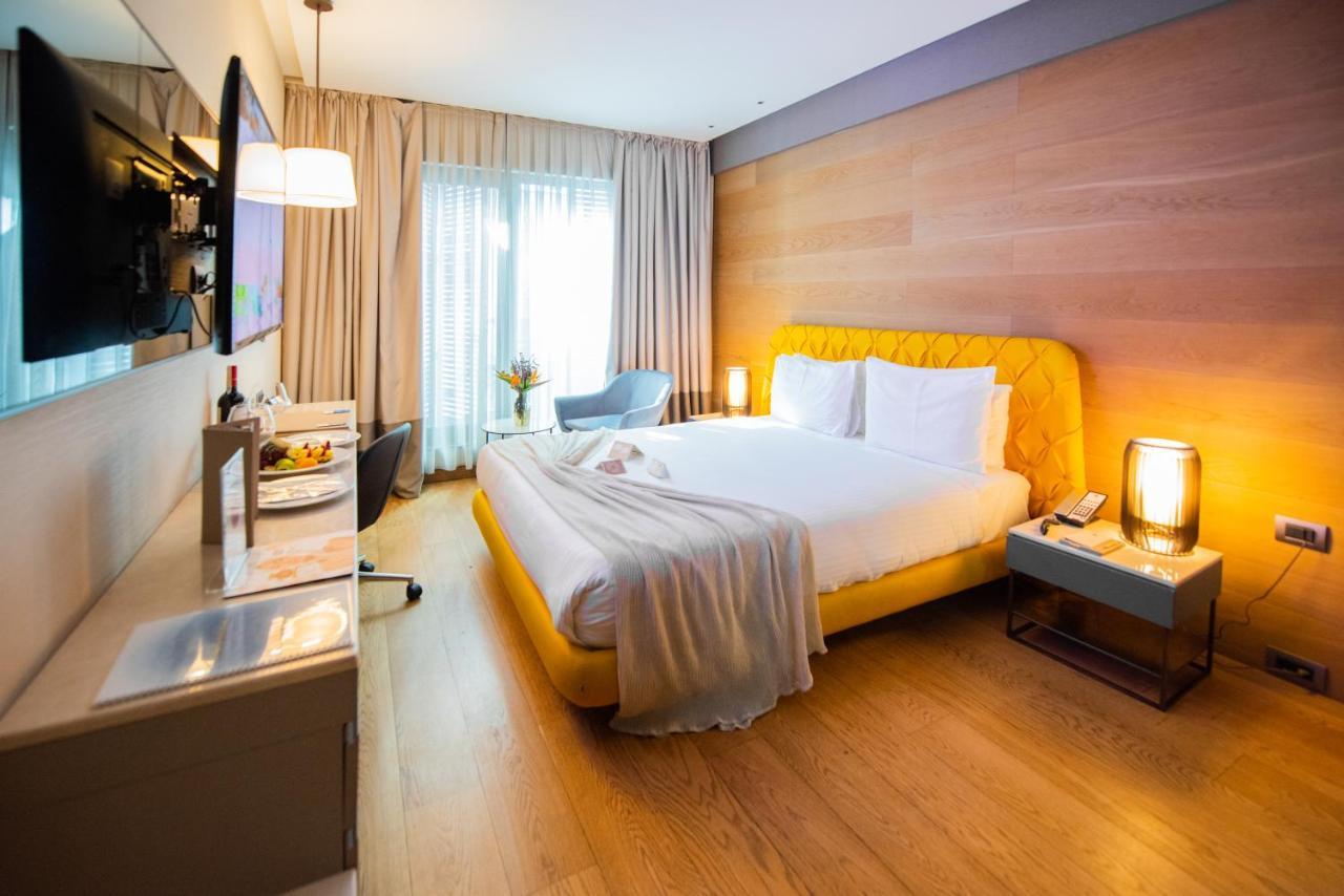 Dosso Dossi Hotels & Spa Downtown Istambul Exterior foto The photo shows a modern hotel room with a cozy and inviting atmosphere. The room features a large bed with a yellow upholstered headboard, topped with white bedding and a soft gray throw blanket casually draped over it. To the side of the bed is a s