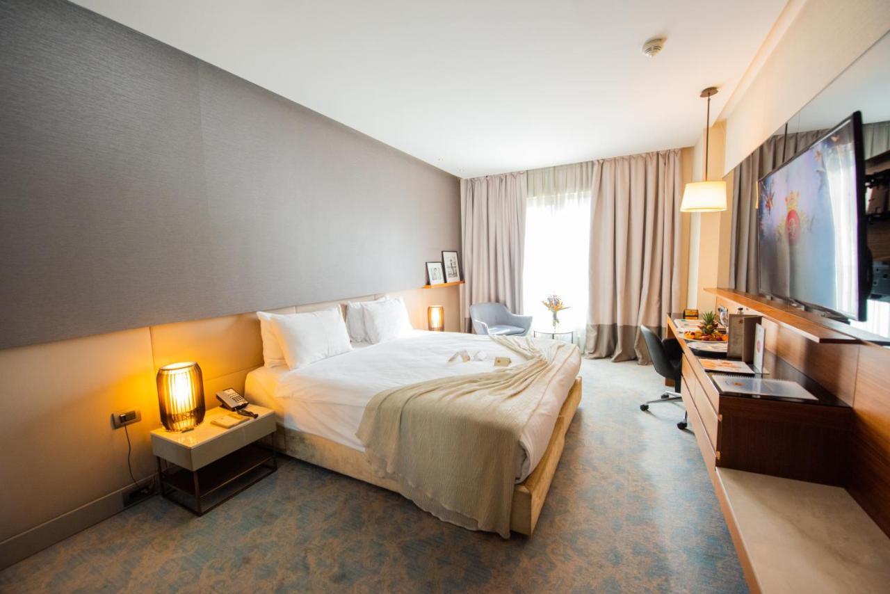 Dosso Dossi Hotels & Spa Downtown Istambul Exterior foto The photo shows a modern hotel room with a comfortable layout. There's a large bed with white linens and a soft throw blanket. Beside the bed, there are bedside tables with lamps. A window covered with sheer curtains allows natural light to enter the