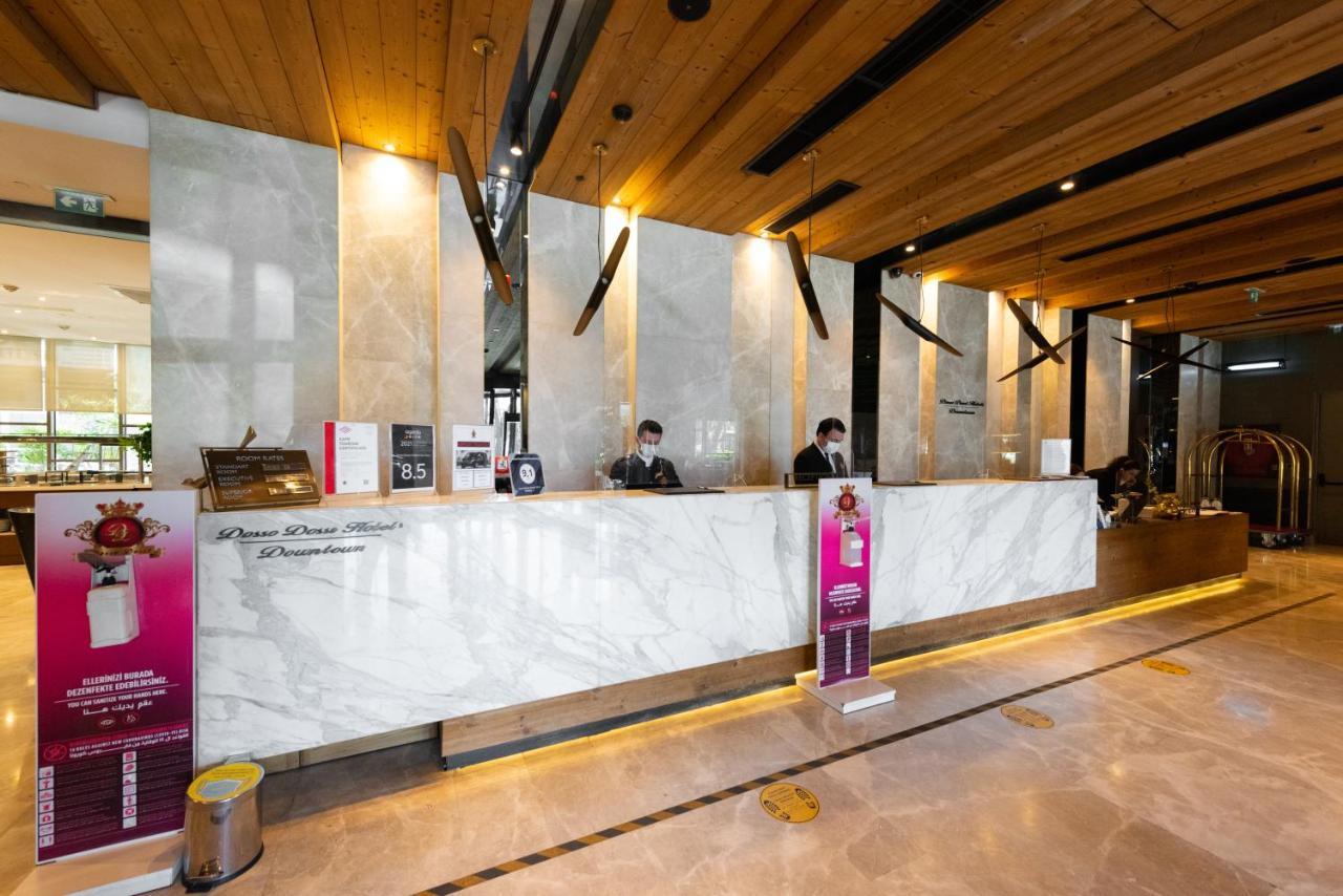 Dosso Dossi Hotels & Spa Downtown Istambul Exterior foto The photo shows a hotel reception area. The front desk is made of elegant marble, and the space features wooden accents on the ceiling. Behind the counter, two staff members are visible, likely assisting guests. There are signs and promotional materi