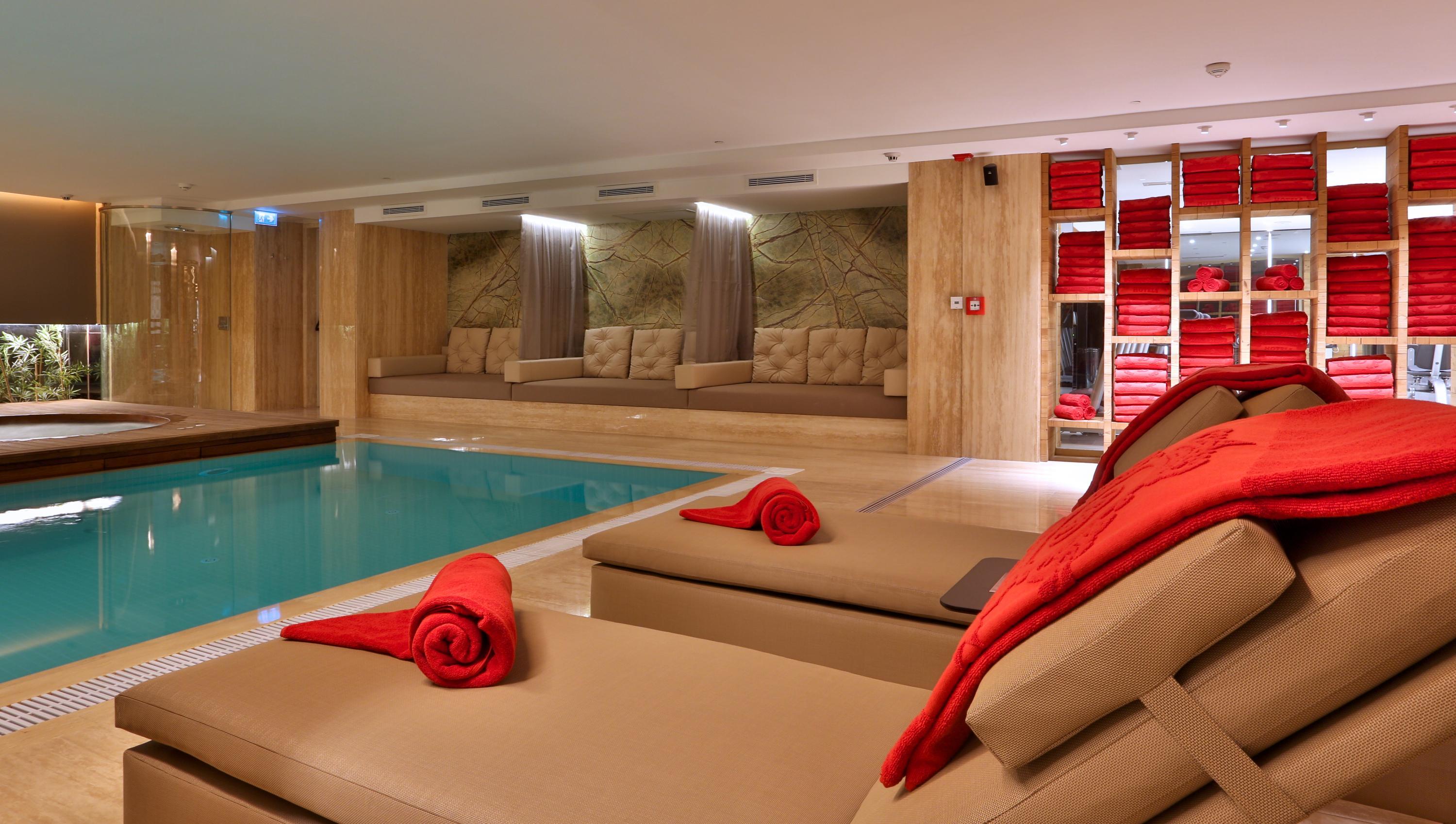 Dosso Dossi Hotels & Spa Downtown Istambul Exterior foto The photo shows a modern, luxurious spa area featuring a swimming pool. In the foreground, there are comfortable lounge chairs with red towels rolled and placed on them. The walls are decorated with wood paneling, and there are several plush seating 