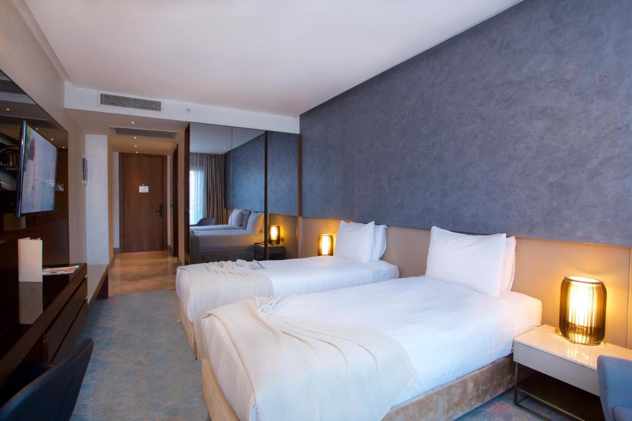 Dosso Dossi Hotels & Spa Downtown Istambul Exterior foto The photo shows a modern hotel room featuring two single beds with white bedding. The walls have a stylish gray finish, and there is a decorative element behind the beds. On either side of the beds, there are bedside tables with lamps. A flat-screen 