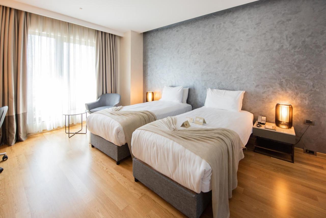 Dosso Dossi Hotels & Spa Downtown Istambul Exterior foto The photo shows a modern hotel room featuring two single beds with white linens and soft gray throw blankets. The room has a stylish design, with wooden flooring and a large window dressed with light curtains that allow natural light to enter. There'