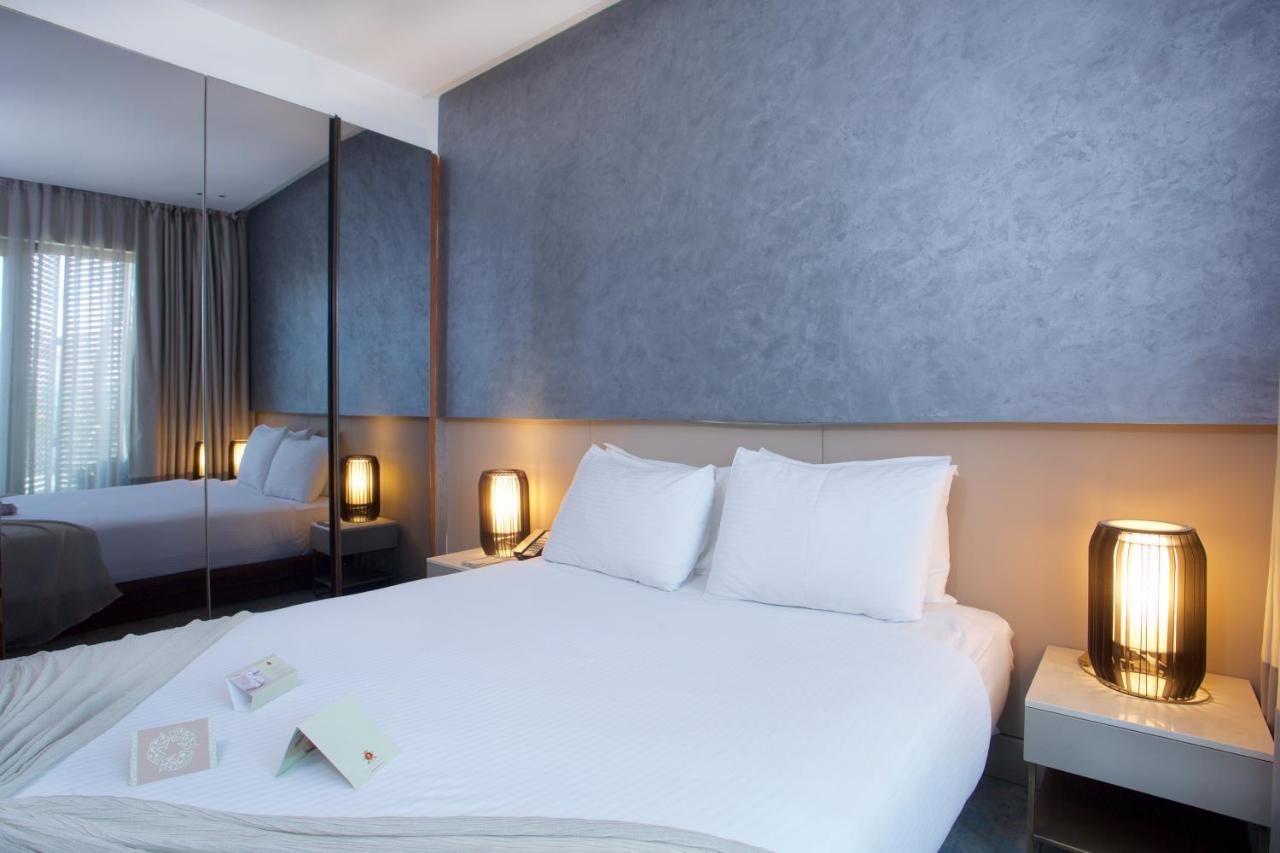 Dosso Dossi Hotels & Spa Downtown Istambul Exterior foto The photo depicts a modern hotel room featuring a double bed with white bedding and two pillows. The walls have a smooth, textured finish, and there are large windows with sheer curtains, allowing natural light to filter in. On either side of the bed