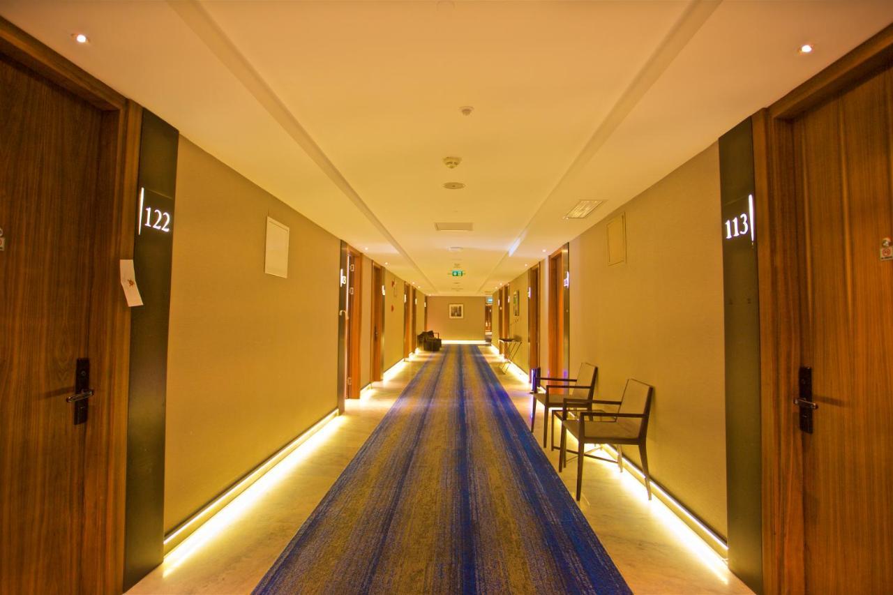 Dosso Dossi Hotels & Spa Downtown Istambul Exterior foto The photo shows a hotel corridor with several wooden doors on either side. Each door is numbered, with numbers visible for rooms 113 and 122. The hallway features a long blue rug running down the center and has soft lighting along the sides, creating