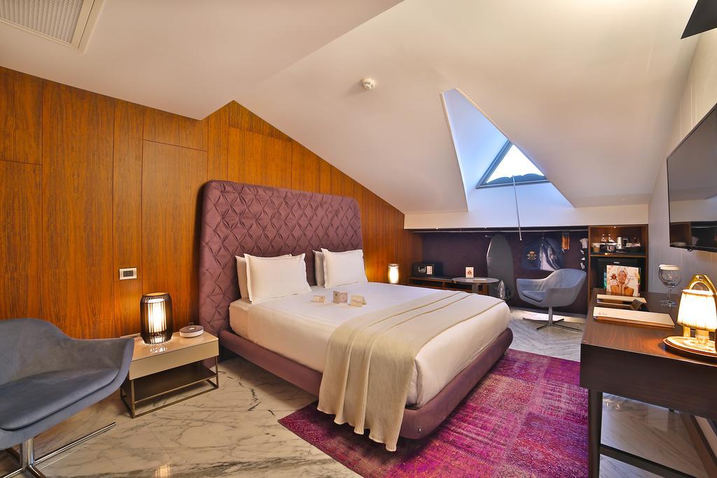Dosso Dossi Hotels & Spa Downtown Istambul Exterior foto The photo shows a modern hotel room featuring a stylish design. It has a large bed with a purple headboard, neatly made with white bedding. The walls are a warm wooden tone, and the room has slanted ceilings with a skylight that lets in natural light